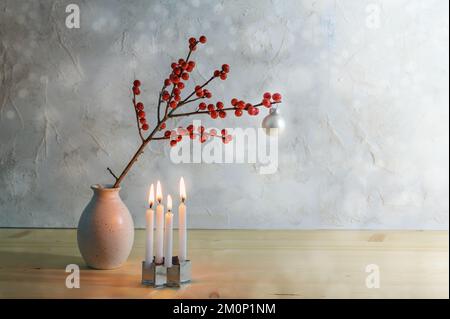 Minimalistischer vierter Adventszug mit vier kleinen brennenden Kerzen und einem Beerenzweig mit einem weißen weihnachtsball in einer Vase, verschneitem Hintergrund mit Kopierraum, s. Stockfoto