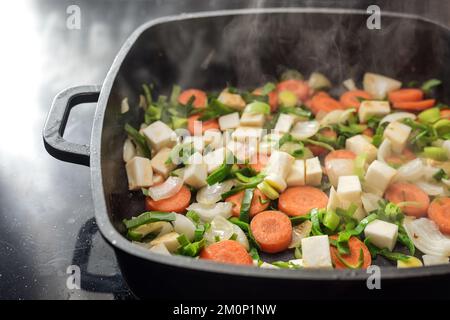 Dampfgaren von gehacktem Gemüse in einer schwarzen Kochschale, Zutaten für Suppen oder Soßen mit Karotten, Zwiebeln, Lauch und Sellerie, Kopierbereich, ausgewählter Fokus Stockfoto