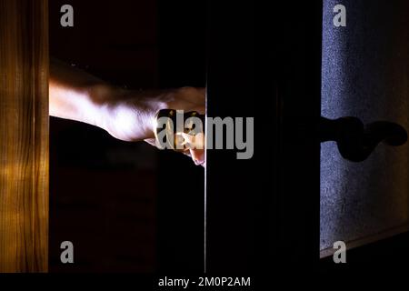 Die Hand einer Frau öffnet zu Hause im Dunkeln die Tür, Türknauf Stockfoto
