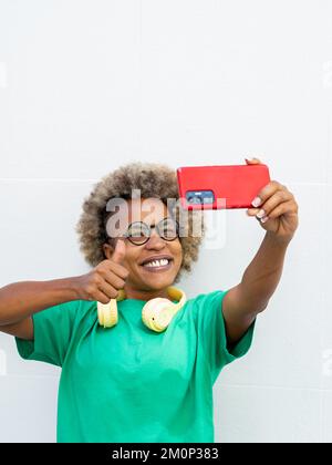 Lächelnde junge afroamerikanische Frau mit Afro-Haaren und Kopfhörern beim Selfie Stockfoto