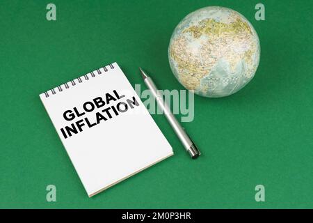 Globales Konzept. Auf einer grünen Oberfläche liegt ein Modell des Planeten und ein Notizblock mit der Inschrift "Globale Inflation" Stockfoto