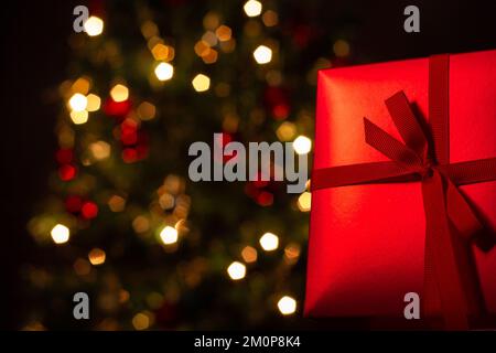 Goiânia, Goias, Brasilien – 07. Dezember 2022: Eine Geschenkbox, rot, mit Schleife und einem Weihnachtsbaum im Hintergrund. Stockfoto