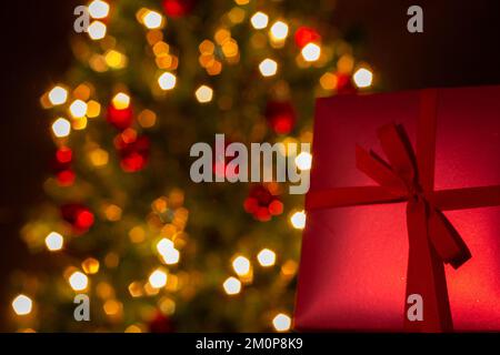 Goiânia, Goias, Brasilien – 07. Dezember 2022: Eine Geschenkbox, rot, mit Schleife und einem Weihnachtsbaum im Hintergrund. Stockfoto