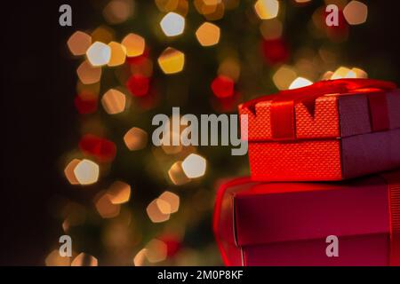 Goiânia, Goias, Brasilien – 07. Dezember 2022: Zwei Geschenkschachteln, rot, mit Schleife und einem Weihnachtsbaum im Hintergrund. Stockfoto