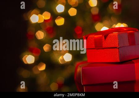 Goiânia, Goias, Brasilien – 07. Dezember 2022: Zwei Geschenkschachteln, rot, mit Schleife und einem Weihnachtsbaum im Hintergrund. Stockfoto