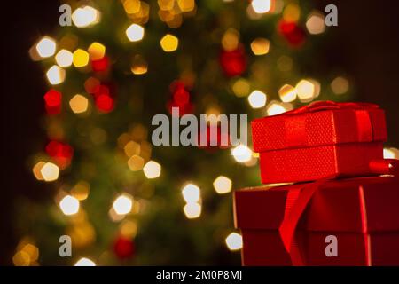 Goiânia, Goias, Brasilien – 07. Dezember 2022: Zwei Geschenkschachteln, rot, mit Schleife und einem Weihnachtsbaum im Hintergrund. Stockfoto