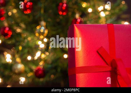 Goiânia, Goias, Brasilien – 07. Dezember 2022: Eine Geschenkbox, rot, mit Schleife und einem Weihnachtsbaum im Hintergrund. Stockfoto