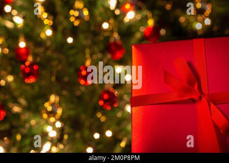 Goiânia, Goias, Brasilien – 07. Dezember 2022: Eine Geschenkbox, rot, mit Schleife und einem Weihnachtsbaum im Hintergrund. Stockfoto