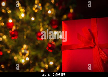 Goiânia, Goias, Brasilien – 07. Dezember 2022: Eine Geschenkbox, rot, mit Schleife und einem Weihnachtsbaum im Hintergrund. Stockfoto