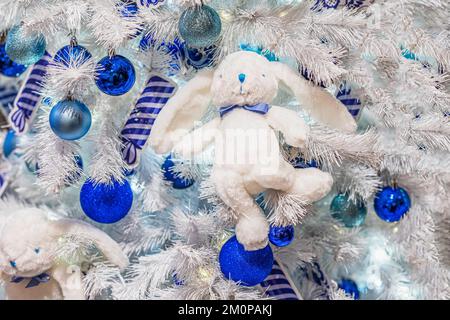 Weihnachtsbaumschmuck in Form von flauschigen, weißen Kaninchenspielzeug und glitzernden Kugeln. Abstrakter Weihnachtshintergrund. Frohe Weihnachten und frohes neues Jahr, Stockfoto