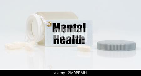Medizin und Gesundheitskonzept. Auf einem weißen reflektierenden Hintergrund gibt es Pillen und ein Glas mit Drogen mit einem Tag, auf dem steht - mentale Gesundheit Stockfoto