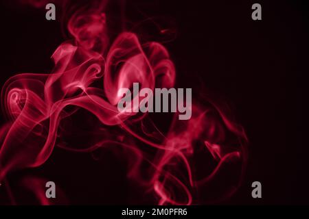 Rote Rauchspuren auf schwarzem Hintergrund. Farbe des Jahres 2023 - Viva Magenta Stockfoto