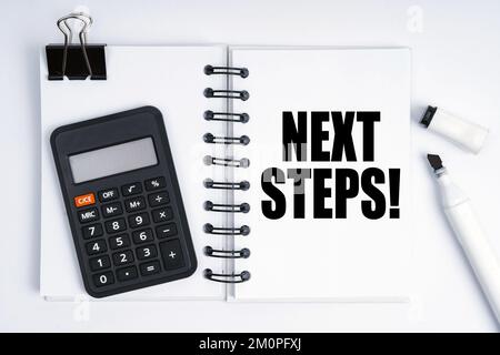 Wirtschafts- und Finanzkonzept. Auf der Tabelle befinden sich ein Marker, ein Taschenrechner und ein Notizbuch mit der Aufschrift „Next Steps“ (Nächste Schritte) Stockfoto
