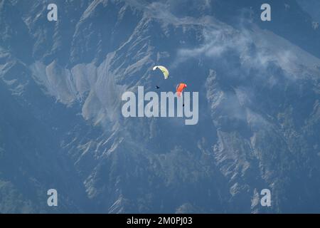 Zwei Gleitschirmfliegen in unmittelbarer Nähe des anderen, hoch über dem Boden vor dem Hintergrund eines dunklen Berges im Mont Blanc ma Stockfoto