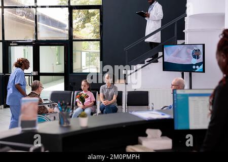 Arzthelferin bringt älteren Patienten zur Familie nach Abschluss der medizinischen Beratung, Enkelin hält Blumenstrauß für Großmutter. Menschen stehen in der Krankenhauslobby. Medizindienst Stockfoto