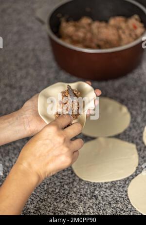 Frauenhände füllen eine argentinische Fleischempanada. Stockfoto