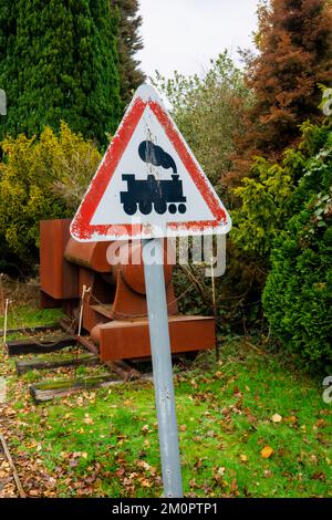 Ein klassisches weißes Schild mit rotem dreieckigen Grenzübergangsschild mit einem Warnbild eines Zuges bei der Mizens Railway in Knaphill, Woking, Surrey Stockfoto