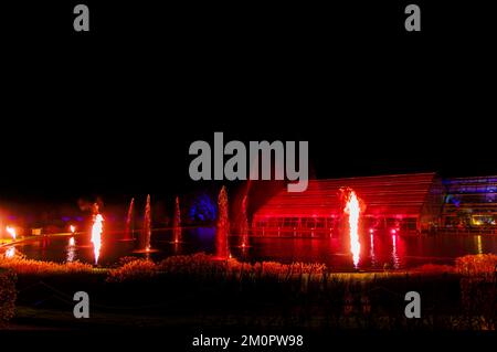 Das Glasshouse und der See werden im jährlichen Weihnachtsglühen 2022, RHS Garden Wisley, Surrey, mit bunten Lichtern bei Nacht beleuchtet Stockfoto