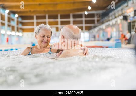 Ein reizendes, älteres, weißes Paar, das seine freie Zeit in einem heißen Bad und einem Pool-Komplex verbringt. Perspektive der Wasseroberfläche. Hochwertiges Foto Stockfoto