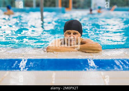 Gesundheitsfürsorge und aktives Körperpflegekonzept. Innenporträt einer freundlichen weißen Rentnerin mit schwarzer Badekappe, die sich im Swimmingpool entspannen kann. Hochwertiges Foto Stockfoto