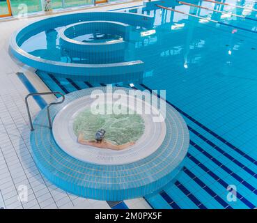 Von oben aus hat man einen runden Whirlpool in einem Schwimmbadkomplex, in dem eine nicht erkennbare Kaukasierin saß. Möglichkeiten der Entspannung. Hochwertiges Foto Stockfoto