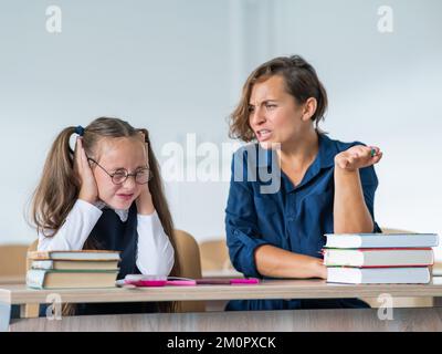 Eine Lehrerin schreit eine Schülerin an. Das kleine Mädchen bedeckt ihre Ohren mit den Händen. Stockfoto