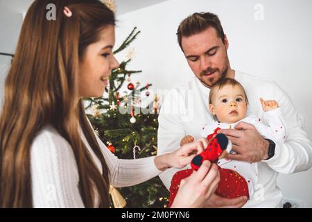 Mom zieht ihr Weihnachtssocken an, während Dad sie hält Stockfoto