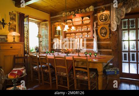 Antiker Tisch und Stühle mit hoher Rückenlehne im rustikalen Speisesaal im Inneren von 1977 erbauten Nachbau der alten Blockhütte im Canadiana Cottage-Stil aus dem Jahr 1800er. Stockfoto