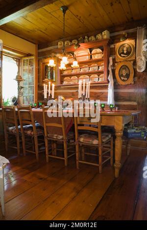 Antiker Tisch und Stühle mit hoher Rückenlehne im rustikalen Speisesaal im Inneren von 1977 erbauten Nachbau der alten Blockhütte im Canadiana Cottage-Stil aus dem Jahr 1800er. Stockfoto