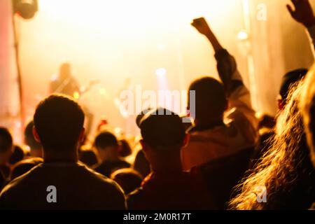 Unschärfe-Jubel und Bühnenbeleuchtung mit Platz für Ihren Text. Die Silhouette der Menschen hebt die Hand in einem Musikkonzert mit schwarzem und gelbem Farbfleck Stockfoto