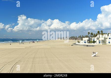 HUNTINGTON BEACH, KALIFORNIEN - 7. DEZ. 2022: Zwei Surfer, die ihre Boards in Huntington Beach in den Sand schleppen. Stockfoto