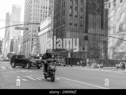 Ein asiatischer Mann fährt seinen Roller auf den Straßen von New York City mit den Wolkenkratzern von Manhattan im Hintergrund. Schwarz-weiße Straßenfotografie Stockfoto