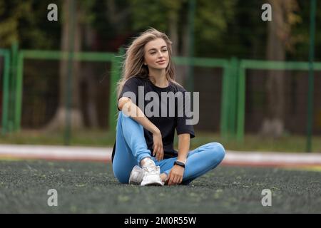Schlanke blonde Frau in Sportbekleidung, die auf dem Fußballfeld sitzt Stockfoto