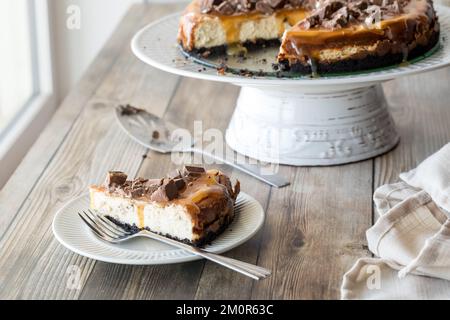 Ein Stück cremigen Käsekuchen mit Karamellsauce und Schokoladenstückchen. Stockfoto