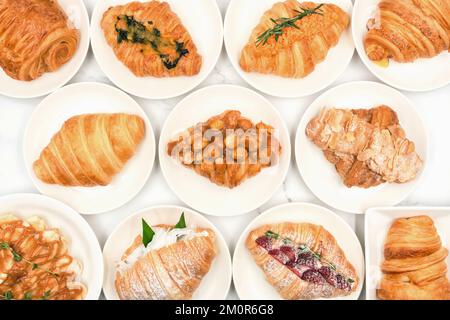 Draufsicht auf frisch gebackene leckere Croissants, verschiedene Arten und Geschmacksrichtungen auf weißem Teller, hausgemachte Isolate mit weißem Hintergrund. Französisches Gebäck. Tradi Stockfoto