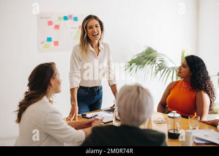 Fröhliche Geschäftsfrau, die eine Besprechung in einem Sitzungssaal leitet. Glückliche junge Geschäftsfrau, die mit ihren Kollegen Brainstorming führt. Gruppe multikultureller Geschäftsleute Stockfoto