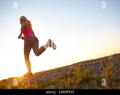 Sie rennt ihr Herz raus. Eine wunderschöne junge Frau, die joggt, während die Sonne vor ihr untergeht. Stockfoto