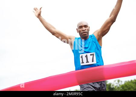 Das Ende ist ein Sieg. Verkürzte Vorderansicht eines männlichen Athleten, der ein Rennen mit erhobenen Armen gewinnt. Stockfoto