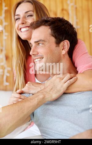Du fühlst dich wie zu Hause für mich... Ein glückliches junges Paar, das auf der Couch sitzt und sich liebevoll umarmt. Stockfoto