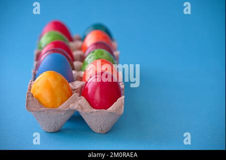 Bunte Ostereier in Pappkarton auf blauem Hintergrund Stockfoto