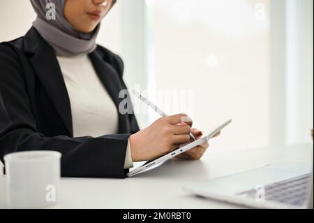 Nahaufnahme einer professionellen und wunderschönen muslimischen Geschäftsfrau, die ein digitales Tablet am Schreibtisch verwendet. Stockfoto