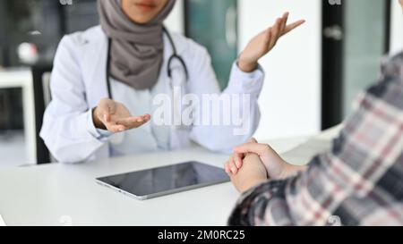 Zugeschnittenes Bild, Eine professionelle asiatische muslimische Ärztin, die mit einem Patienten in der Praxis spricht, erklärt Krankenversicherungsleistungen, gibt einen Arzt Stockfoto