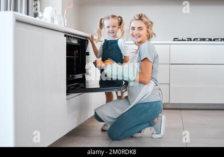 Lächelnde Mutter und Tochter, die zusammen backen. Glückliche Eltern und Kinder halten ein Tablett mit gebackenen Muffins. Eine weiße Frau, die frische, gebackene Muffins herausnimmt Stockfoto
