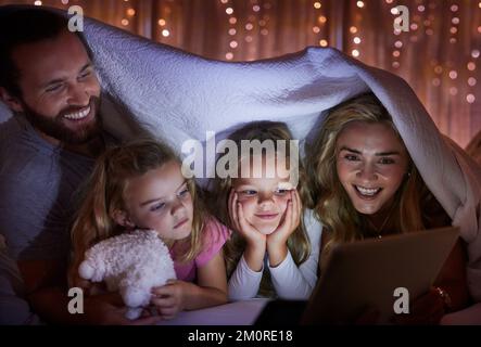 Junge, weiße Familie, die ein digitales Tablet zusammen unter einer Decke zu Hause benutzt. Kleine Geschwister, die sich entspannen und mit denen sie einen Film anschauen Stockfoto