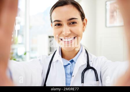 Porträt einer jungen Ärztin gemischter Rasse, die ein Selfie macht, während sie lächelt und ein Stethoskop in einer Krankenhauspraxis trägt Stockfoto