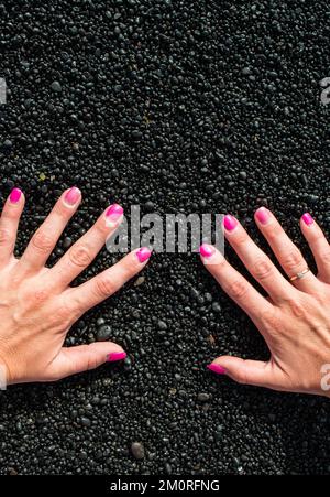 Hände und rosa Nägel am schwarzen Strand von Lanzarote Stockfoto