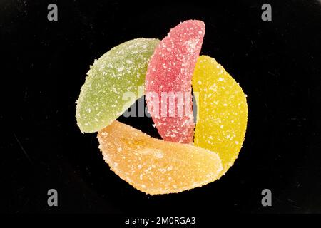 Vier süße Marmeladen-Süßigkeiten auf einer schwarzen Keramikplatte, Makro, Draufsicht. Stockfoto