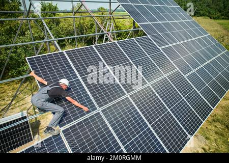 Arbeiter, der Sonnenkollektoren im Feld an sonnigen Tagen installiert. Europäischer Mann mit Helm und Uniform. Photovoltaiksammlung von Modulen als PV-Panel. Konzept der Umweltsicherheit. Grüne Energie. Stockfoto