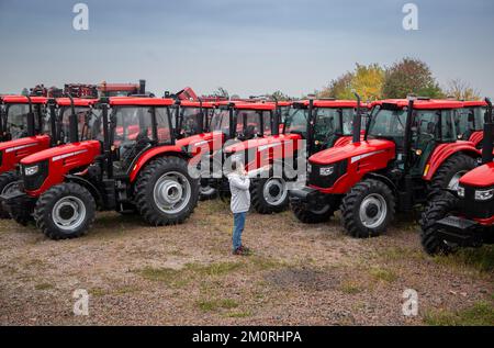 Präsentation und Verkauf neuer roter Traktoren in Folge. Ein Mann spricht am Telefon und zeigt auf einen der landwirtschaftlichen Traktoren. Ausrüstung für einen Stockfoto