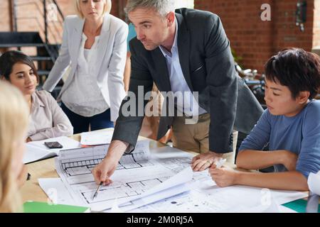 Der Kunde möchte, dass wir diesen Abschnitt überarbeiten. Eine Gruppe von Architekten, die mit Bauplänen in einem Büro arbeiten. Stockfoto